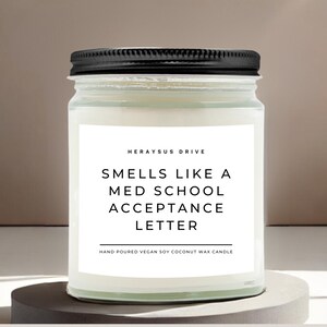 May include: A white candle in a glass jar with a black lid. The label reads "HERAYSUS DRIVE SMELLS LIKE A MED SCHOOL ACCEPTANCE LETTER HAND POURED VEGAN SOY COCONUT WAX CANDLE".