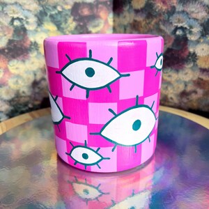 May include: Pink ceramic planter with a checkered pattern and white eyes with green pupils.
