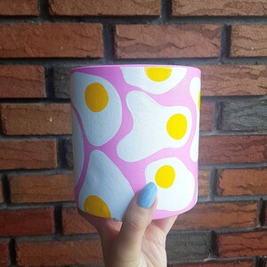 Peut inclure: Pot en céramique rose avec un motif d'œuf au plat blanc et jaune.