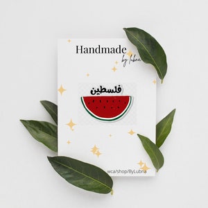 May include: Handmade watermelon sticker with the Arabic text "Watermelon" in yellow. The sticker is on a white card with a gold star pattern. The card also has the text "Handmade by Lubna" and "wca/shop/ByLubna".