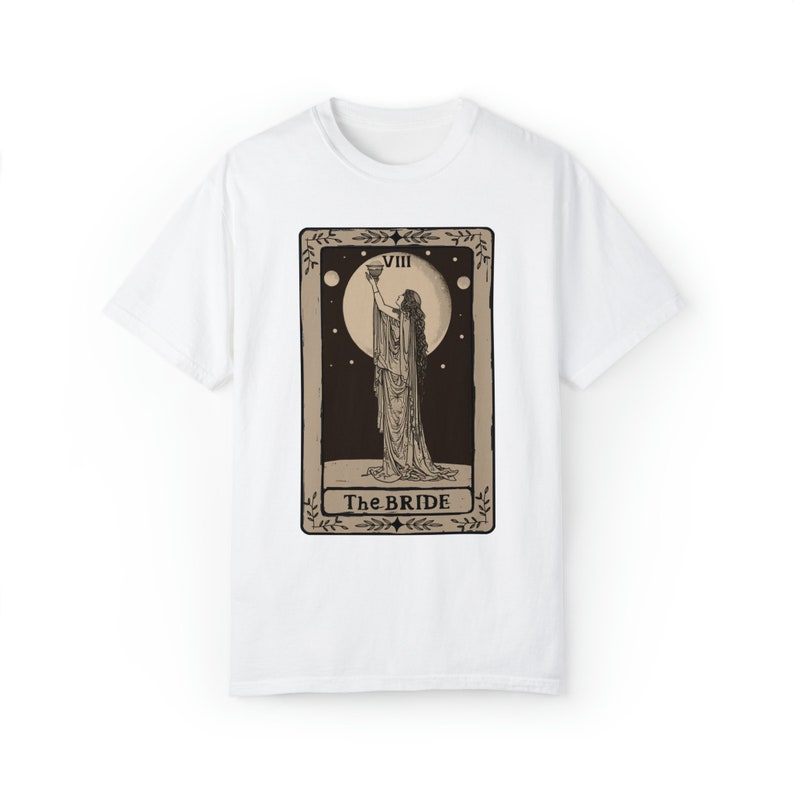 Op de afbeelding: Wit T-shirt met een bruin tarotkaartontwerp met een vrouw die een beker vasthoudt en de tekst "VIII The BRIDE".