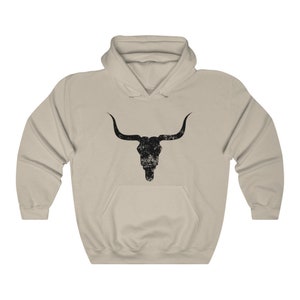 Pu&ograve; includere: Una felpa con cappuccio beige con una grafica di teschio di toro nero invecchiato sul davanti.