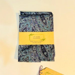 Op de afbeelding: Een set van twee blauwe paisley-gepatroneerde zakdoeken gemaakt van 100% biologisch katoen. De zakdoeken zijn gevouwen en op elkaar gestapeld. Een klein bruin label met de tekst "C's Crafts #handmade" is aan de zakdoeken bevestigd.