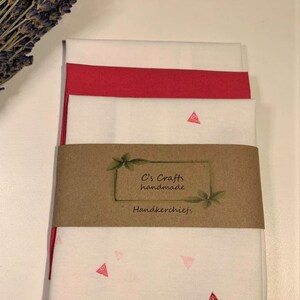 May include: Set of three white handkerchiefs with pink triangle designs. The handkerchiefs are folded and stacked, with a brown paper label that reads "C's Crafts handmade handkerchiefs".