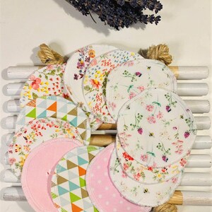 May include: A set of 10 reusable cotton rounds with various floral and geometric patterns. The rounds are white with a white trim and are arranged in a circle on a wooden surface.