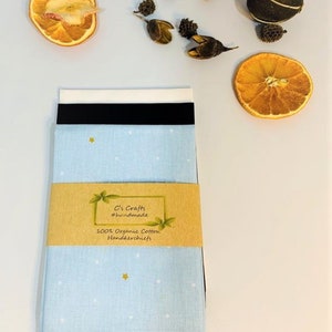 May include: A set of three blue handkerchiefs with a white and gold star pattern. The handkerchiefs are packaged in a brown paper wrapper with a label that reads "C's Crafts #handmade 100% Organic Cotton Handkerchiefs".