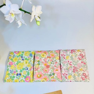May include: Three small fabric pouches with floral patterns. The pouches are lined up in a row on a white surface. The pouch on the left has a yellow floral pattern, the middle pouch has a pink floral pattern, and the pouch on the right has a pink and white floral pattern. A small brown tag with the text "C's Crafts #handmade" is in the lower right corner of the image.