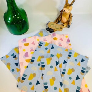 May include: A stack of four blue and pink fabric squares with a geometric pattern of circles, semi-circles, and triangles. The squares are made of a soft, textured fabric and are perfect for a variety of uses, such as cleaning, wiping, or as a decorative element.