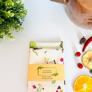 May include: A set of two white cotton handkerchiefs with a floral and mushroom print. The handkerchiefs are packaged with a yellow label that reads "C's Crafts #handmade 100% Cotton Handkerchiefs".