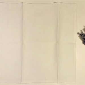 May include: A white cotton tea towel folded in thirds. The towel is plain white with no designs or patterns.