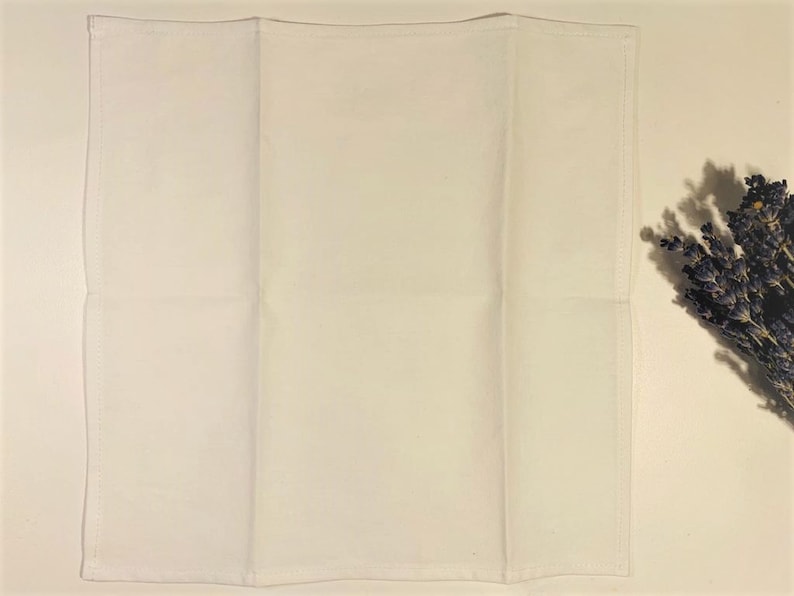 May include: A white cotton tea towel folded in thirds. The towel is plain white with no designs or patterns.