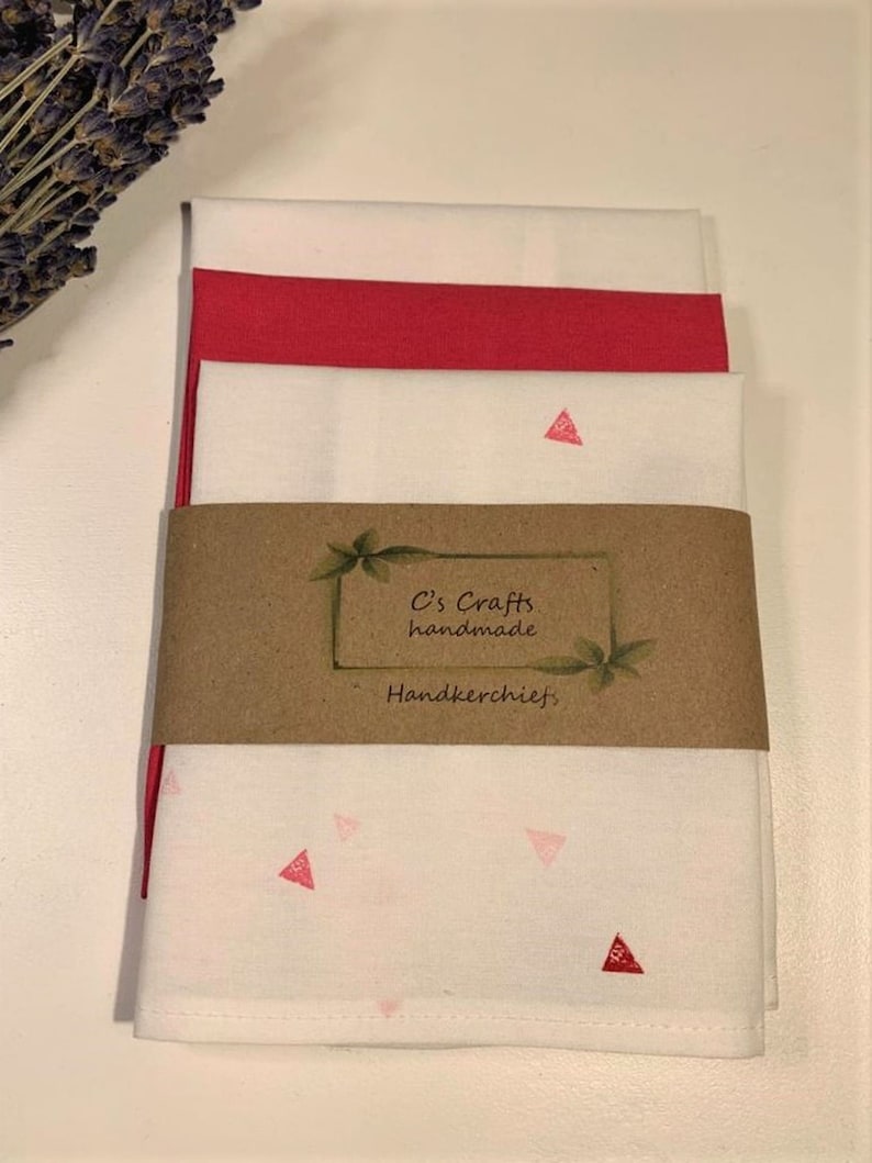 May include: Set of three white handkerchiefs with pink triangle designs. The handkerchiefs are folded and stacked, with a brown paper label that reads "C's Crafts handmade handkerchiefs".