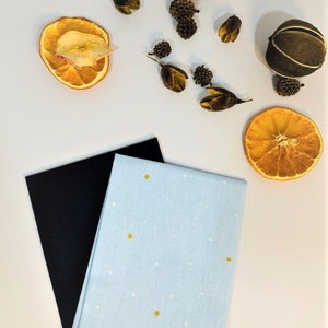 May include: A blue tea towel with white polka dots and gold stars. The tea towel is folded in half and is sitting on top of a black piece of fabric. There are dried orange slices and other decorative items on a white surface.