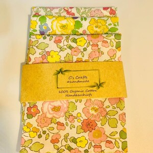 May include: A set of three floral handkerchiefs made from 100% organic cotton. The handkerchiefs are packaged with a brown paper label that reads "C's Crafts #handmade 100% Organic Cotton Handkerchiefs".