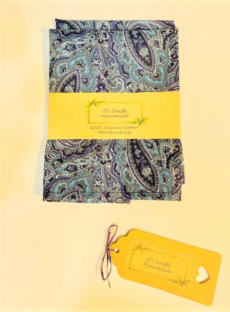 Op de afbeelding: Twee blauwe en paarse paisley-gepatroneerde zakdoeken met een geel label met de tekst "C's Crafts #handmade 100% Organic Cotton Handkerchiefs".