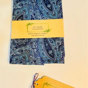 Op de afbeelding: Een blauwe paisley-gepatroneerd zakdoek gemaakt van 100% biologisch katoen. De zakdoek is gevouwen en verpakt met een bruin papieren label waarop "C's Crafts #handmade" staat.