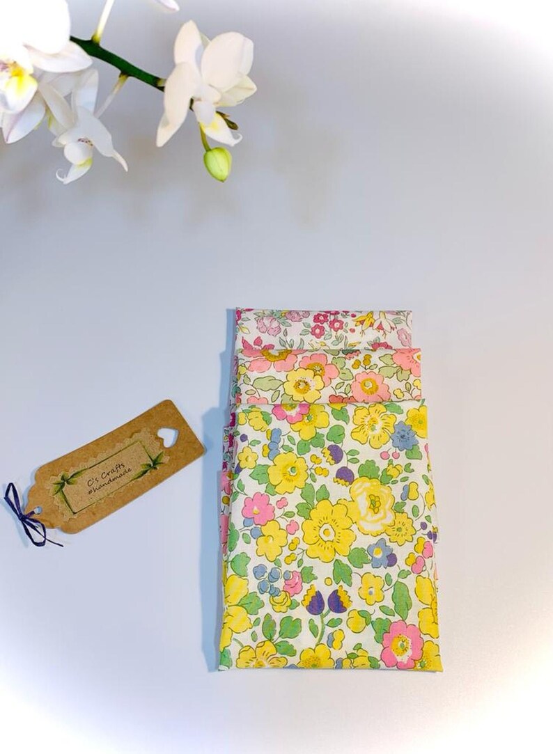 May include: A stack of four fabric squares with a floral pattern in shades of pink, yellow, and green. The fabric squares are folded neatly and have a white background. A small brown tag with the text "C's Crafts & Handmades" is visible in the image.