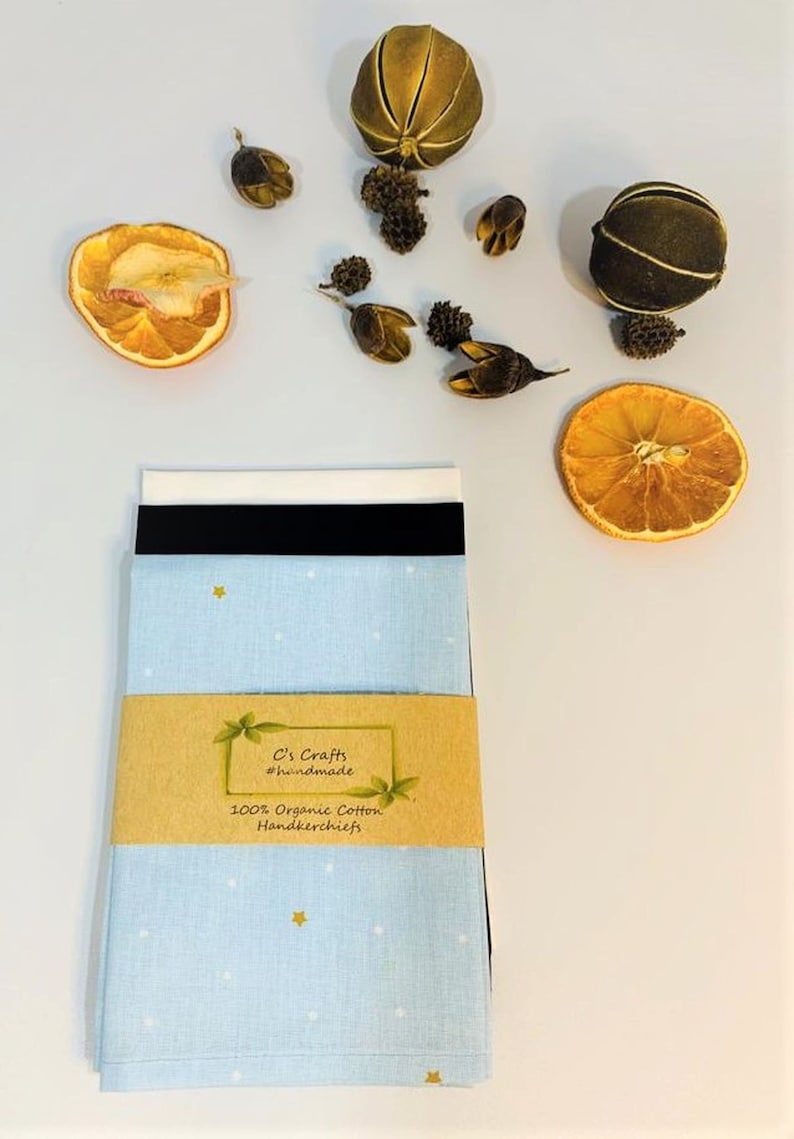 May include: A set of three blue handkerchiefs with a white and gold star pattern. The handkerchiefs are packaged in a brown paper wrapper with a label that reads "C's Crafts #handmade 100% Organic Cotton Handkerchiefs".