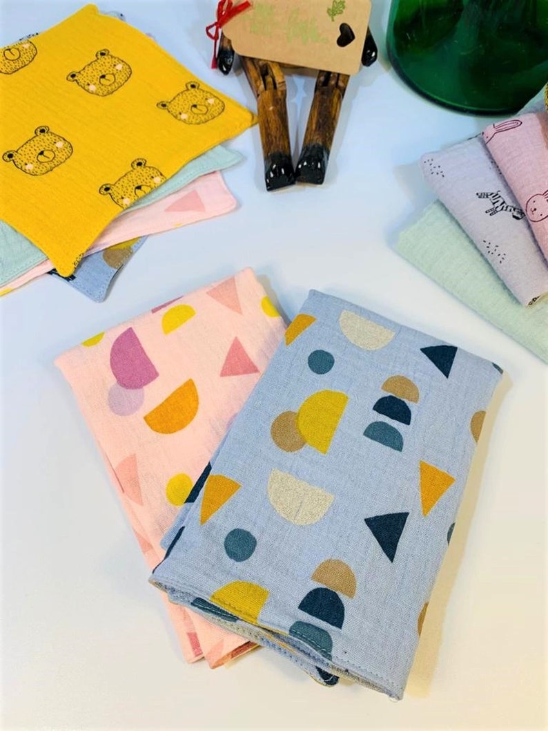 May include: Two folded fabric squares with geometric patterns. One square is light blue with yellow, brown, and dark blue circles and triangles. The other square is pink with yellow, pink, and white circles and triangles.