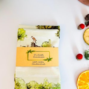 May include: A folded white cotton handkerchief with a green and brown watercolor design of a bird perched on a branch. The handkerchief has a label that reads "C's Crafts #handmade 100% Cotton Handkerchiefs".