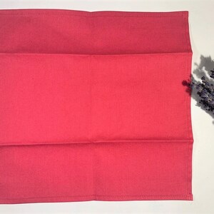 May include: A folded red cotton tea towel. The towel is folded in thirds and has a smooth, even texture.