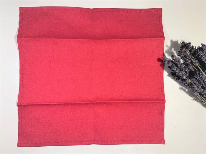 May include: A folded red cotton tea towel. The towel is folded in thirds and has a smooth, even texture.