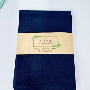 May include: A stack of three dark blue 100% organic cotton handkerchiefs with a brown paper label that reads "C's Crafts #handmade 100% Organic Cotton Handkerchiefs".