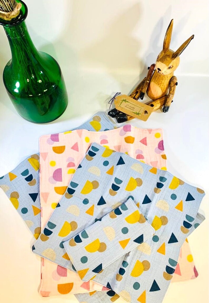 May include: A stack of four blue and pink fabric squares with geometric patterns. The squares are made of a soft, textured material and feature a variety of shapes, including circles, triangles, and semi-circles. The squares are arranged in a staggered pattern, with the largest square at the bottom and the smallest square at the top.