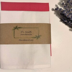 May include: Two folded handkerchiefs, one white and one pink, with a brown paper tag that reads "C's Crafts handmade Handkerchiefs."