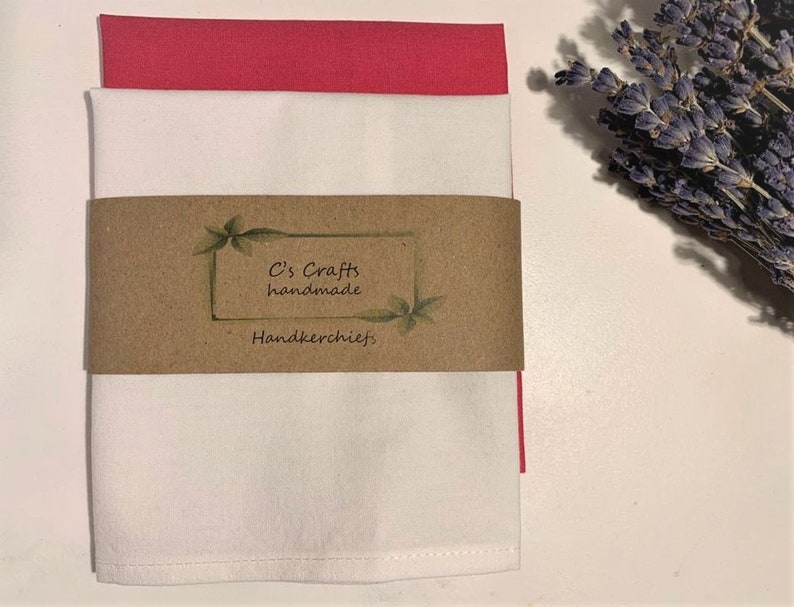 May include: Two folded handkerchiefs, one white and one pink, with a brown paper tag that reads "C's Crafts handmade Handkerchiefs."