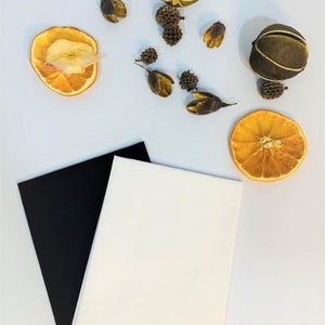 May include: Two pieces of fabric, one black and one white, are laid out on a white surface. Dried orange slices, dried fruit, and dried flower buds are scattered around the fabric.