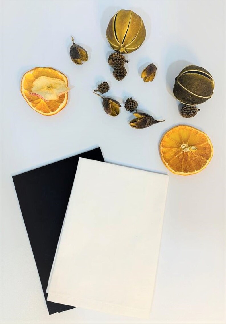 May include: Two pieces of fabric, one black and one white, are laid out on a white surface. Dried orange slices, dried fruit, and dried flower buds are scattered around the fabric.