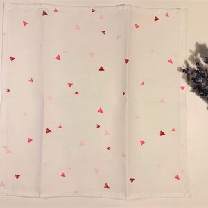 May include: White kitchen towel with a scattered pattern of pink and red triangles.