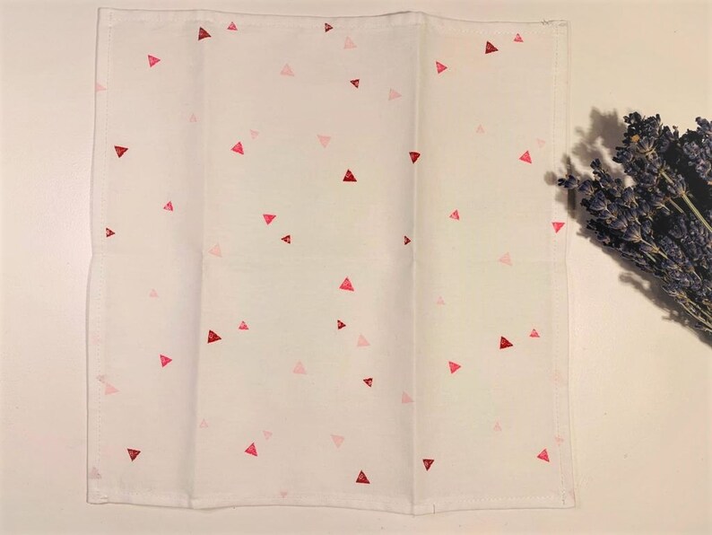 May include: White kitchen towel with a scattered pattern of pink and red triangles.