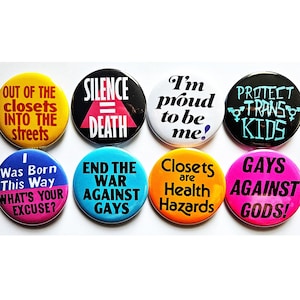 May include: A set of eight circular pin-back buttons featuring various slogans. The buttons display text including "OUT OF THE CLOSETS INTO THE STREETS," "SILENCE = DEATH," "I'm proud to be me!," "PROTECT TRANS KIDS," "I Was Born This Way," and more.