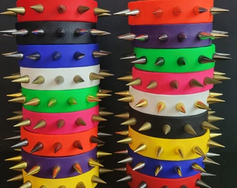 May include: Two stacks of colorful spiked bracelets. The bracelets are made of rubber and have gold-colored spikes. The colors of the bracelets are red, black, blue, white, green, pink, orange, purple, yellow, and blue.