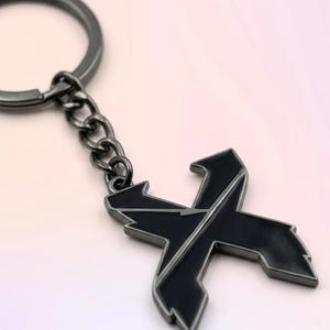 May include: A black metal keychain featuring a stylized letter "X" design. The keychain has a gunmetal finish on the chain and ring. The "X" has a black enamel fill with a silver outline.