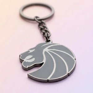 May include: A grey metal keyring with a lion's head design. The lion's head has a white outline and a silver chain and key ring. A stylish accessory.