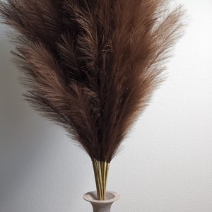 May include: A bouquet of brown pampas grass in a light brown wooden vase. The vase has a wide base and a narrow neck.