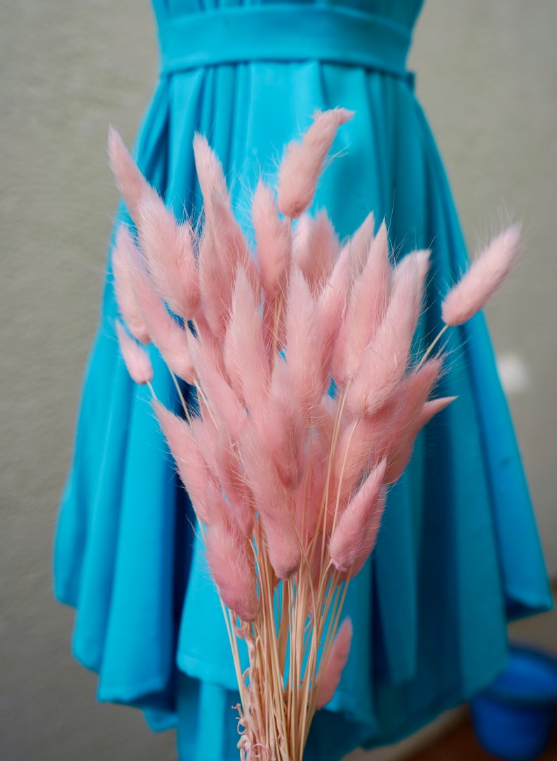 May include: A bouquet of pink bunny tail grass against a bright blue background.