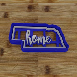 May include: Blue plastic cookie cutter shaped like the state of Nebraska with the word "home" cut out in the center.
