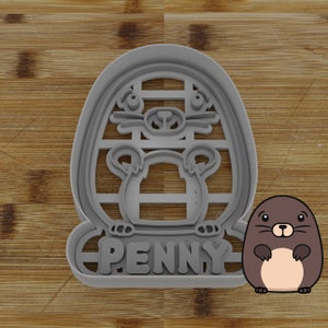 May include: Gray plastic cookie cutter shaped like a cartoon mole with the name "PENNY" underneath. The cutter is on a wooden surface. A cartoon mole is shown next to the cutter.