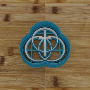 May include: A blue plastic cookie cutter shaped like a cross inside of three overlapping circles. The cross and circles are white.