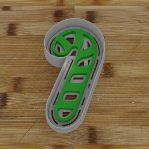 May include: A gray plastic cookie cutter shaped like a candy cane. The cutter has a green outline and a striped design.