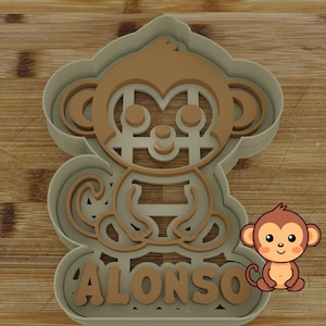 Pode incluir: Um cortador de biscoitos de plástico verde em forma de macaco de desenho animado com o nome "ALONSO" escrito abaixo. O macaco é marrom e tem um grande sorriso.