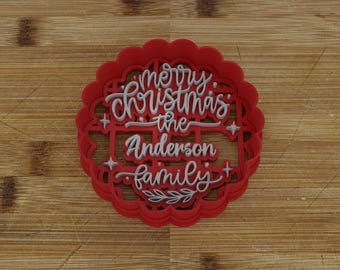 Puede incluir: Cortador de galletas de Navidad de plástico rojo con una inscripción blanca que dice "Feliz Navidad la familia Anderson".