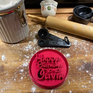 Può includere: Tagliapasta in plastica rossa con le parole "Happy Birthday to Olivia" in un font bianco di scrittura.