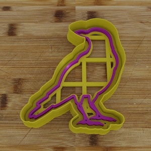 May include: A yellow plastic cookie cutter shaped like a bird. The cutter has a purple outline and is designed to cut out bird-shaped cookies.