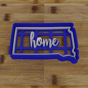 May include: Blue plastic cookie cutter shaped like the state of South Dakota with the word "home" written in white inside.