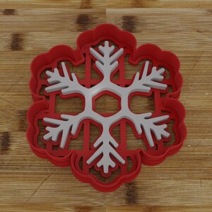 May include: Red plastic snowflake cookie cutter with a white snowflake design.